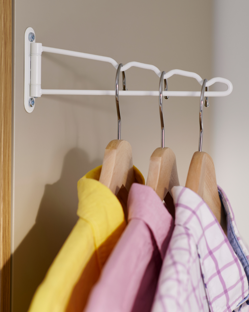 Barra extraíble blanca de clóset con perchas de madera y camisas de colores.