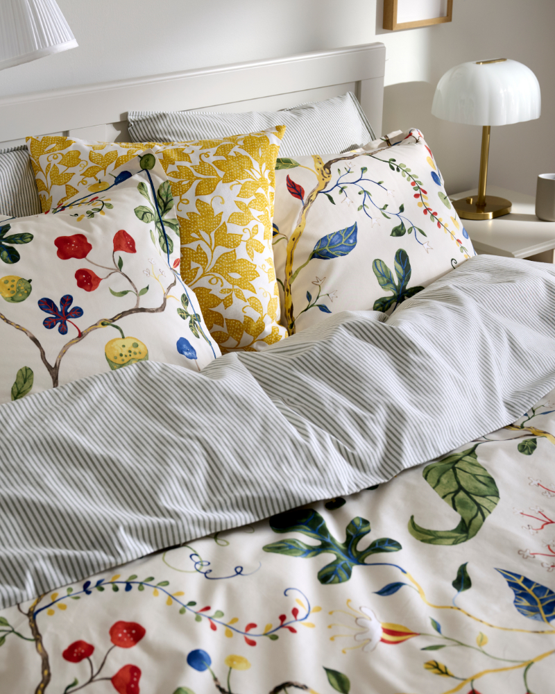 Cama con ropa de cama gris a rayas y cojines florales blancos y amarillos.