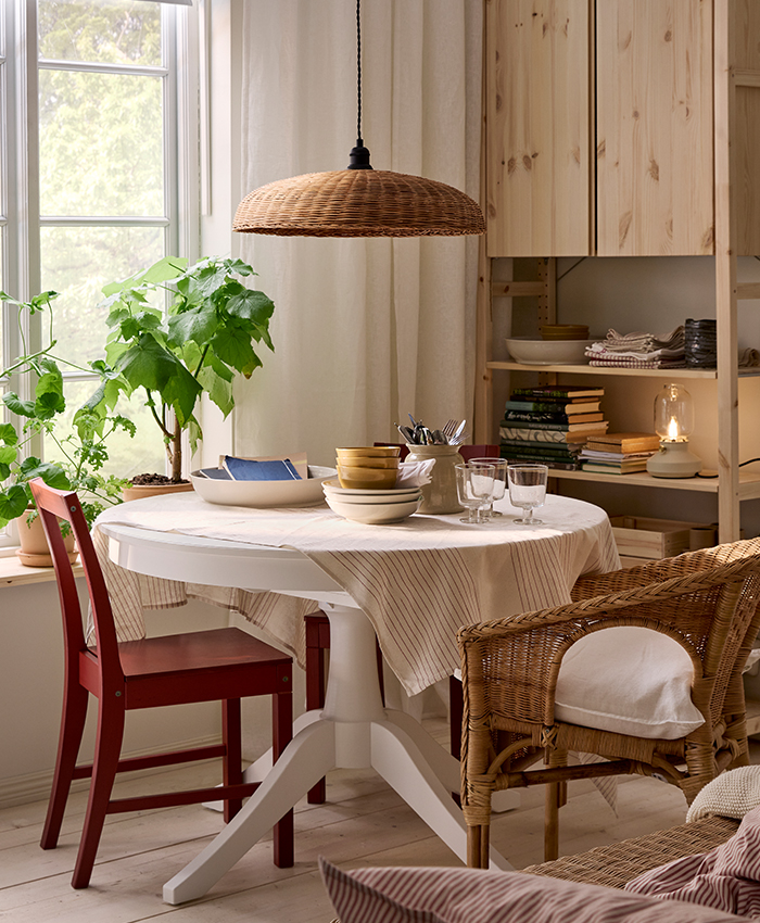 Cosy dining area with an IKEA ROSENTORP extendable table, wooden chairs, tableware and plants by a window.
