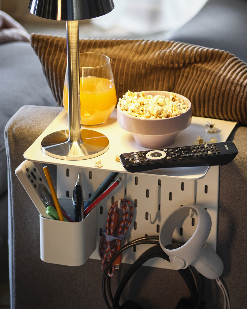 Mesa auxiliar organizadora para reposabrazos en blanco con lámpara, zumo de naranja, tazón de palomitas y mando a distancia.