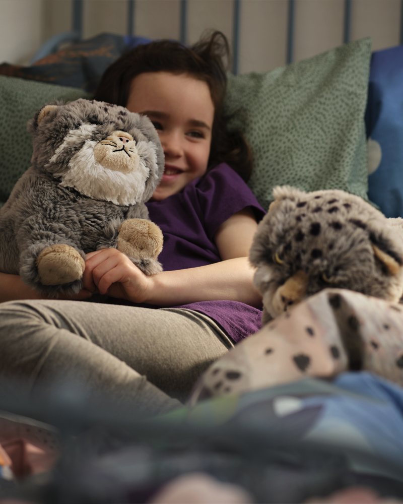 Niña sonriendo mientras juega en la cama con peluches de la colección ALPTALL inspirados en animales del Himalaya.