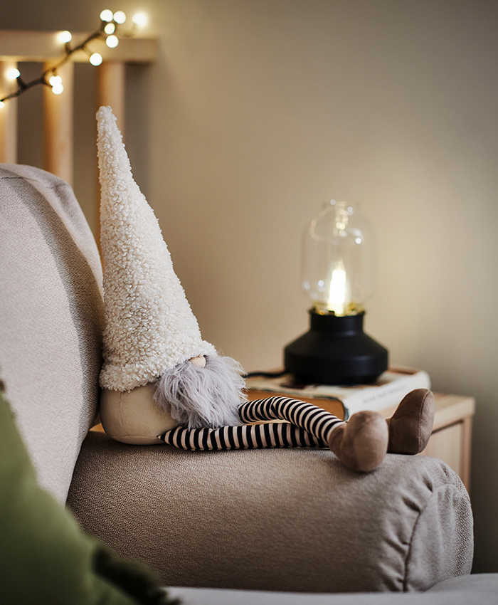 Decoración navideña VINTERFINT de IKEA, con un adorno de un gnomo de textura suave sobre un sofá, acompañado de una lámpara decorativa y luces cálidas