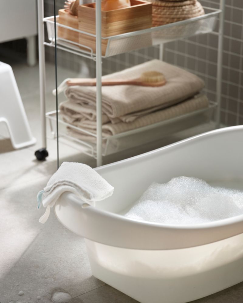 Baño familiar con bañera para bebé LÄTTSAM, carrito HORNAVAN, toallas VÅGSJÖN y cajas de almacenaje DRAGAN.