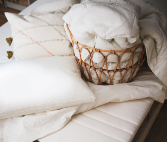 White bedding and pillows beside a wicker basket filled with linens.