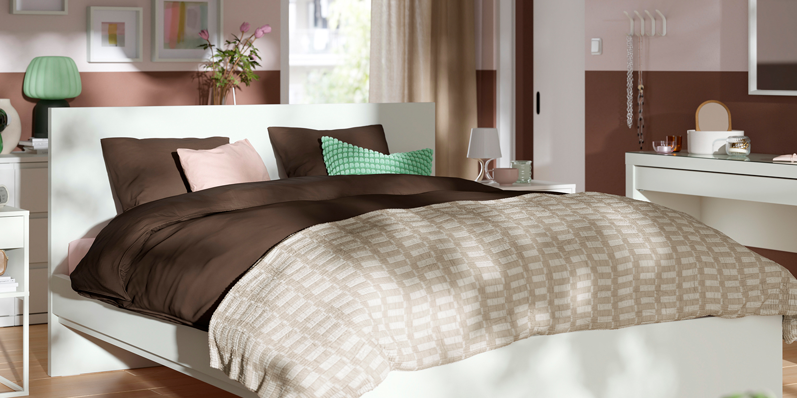 Cama STORKLINTA blanca con cabecero y ropa de cama marrón y beige en dormitorio moderno en tonos rosa y marrón.