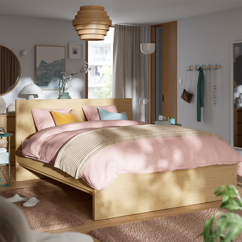 Cama STORKLINTA efecto madera con cabecero, ropa de cama rosa y manta beige en dormitorio moderno y luminoso.