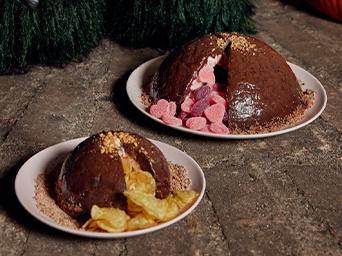 Dos postres de cúpula de chocolate en platos blancos; uno abierto revelando golosinas de corazón rosa y el otro relleno de patatas fritas.