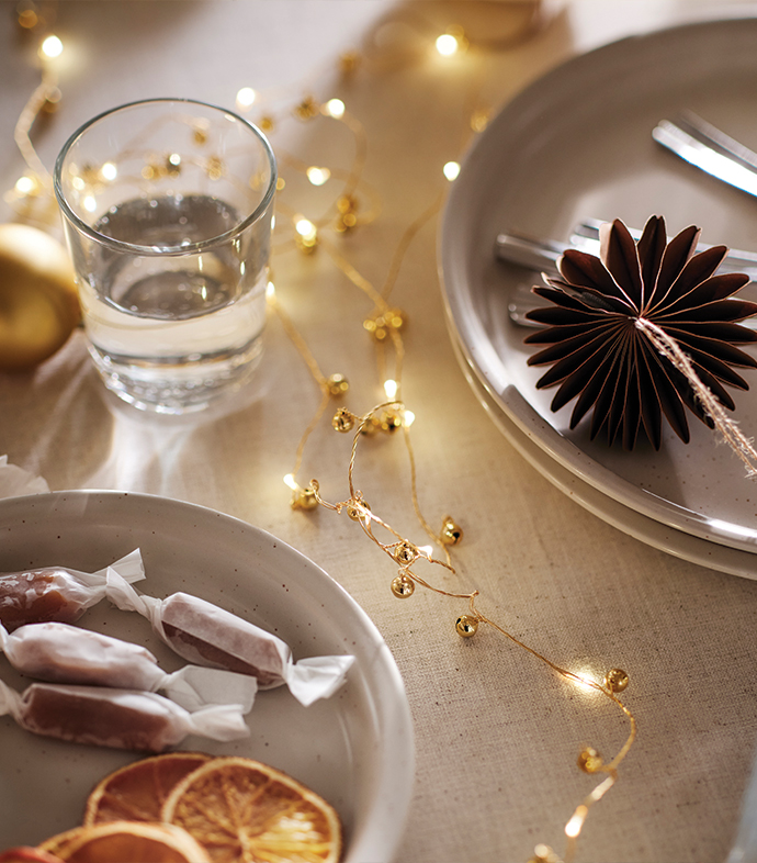 Table set with warm lights, plates, candies, and paper Christmas ornaments.