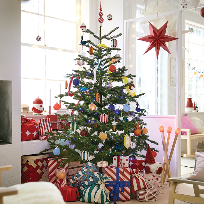 Decorated Christmas tree next to wrapped gifts in a bright room.
