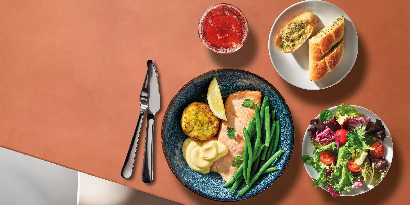 Modern dining setting with SJÖRAPPORT salmon, GRÖNSAKSKAKA veggie medallions, GODMIDDAG plate and MOPSIG cutlery.