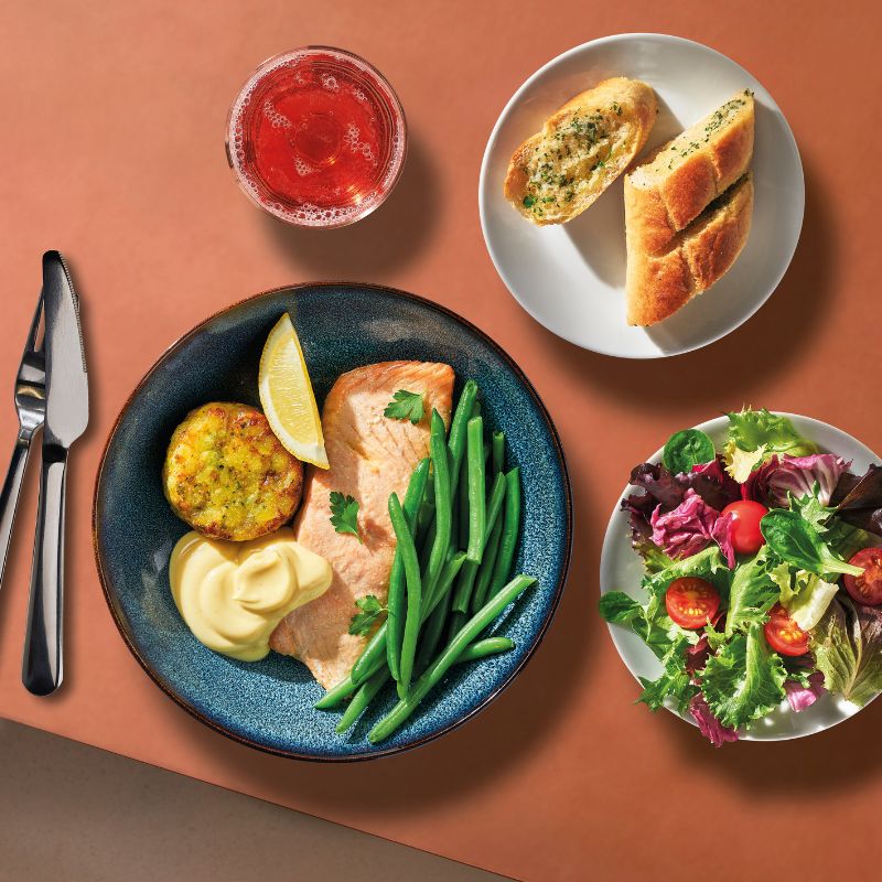 Modern dining setting with SJÖRAPPORT salmon, GRÖNSAKSKAKA veggie medallions, GODMIDDAG plate and MOPSIG cutlery.