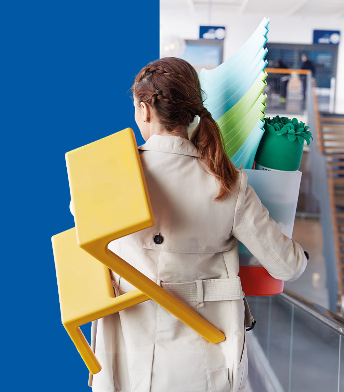 Persona de espaldas cargando un taburete amarillo y una papelera con accesorios coloridos en una tienda IKEA.