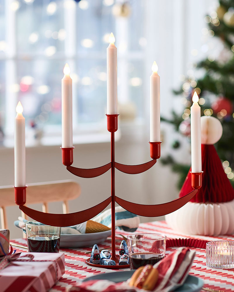 Una vela LED STRÅLA con base roja, acompañada de libros y una decoración VINTERFINT.