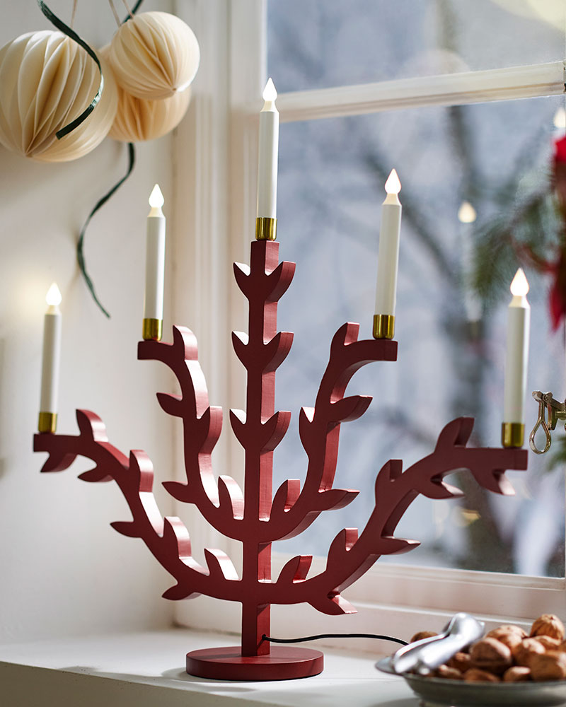 Una vela LED STRÅLA con base verde frente a adornos decorativos sobre una mesa iluminada.