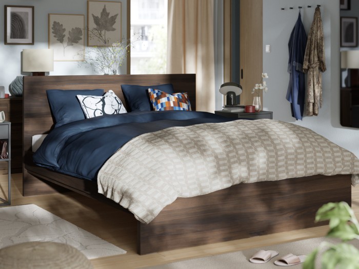 Cama gris con cabezal gris y textiles blancos en una habitacón luminosa.